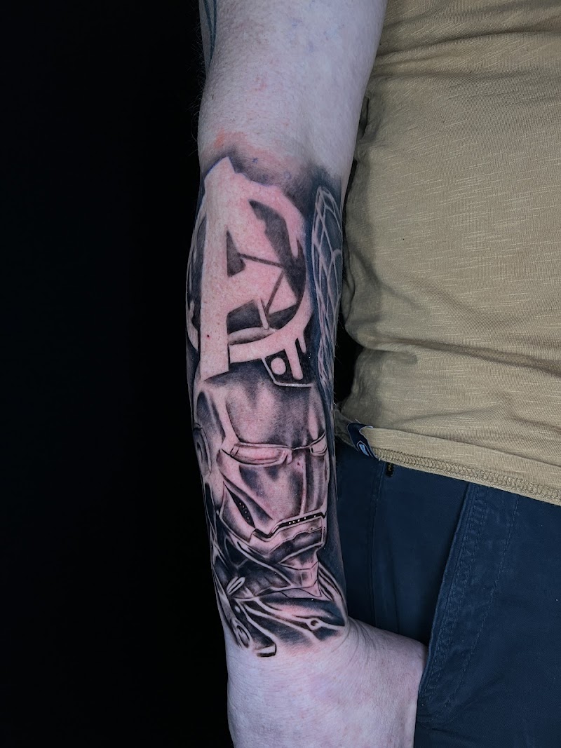 Zwart-wit tattoo van Iron Man en het Avengers logo op de onderarm.