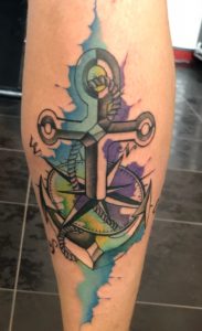 Anker en kompas tattoo met watercolor effect op onderbeen.