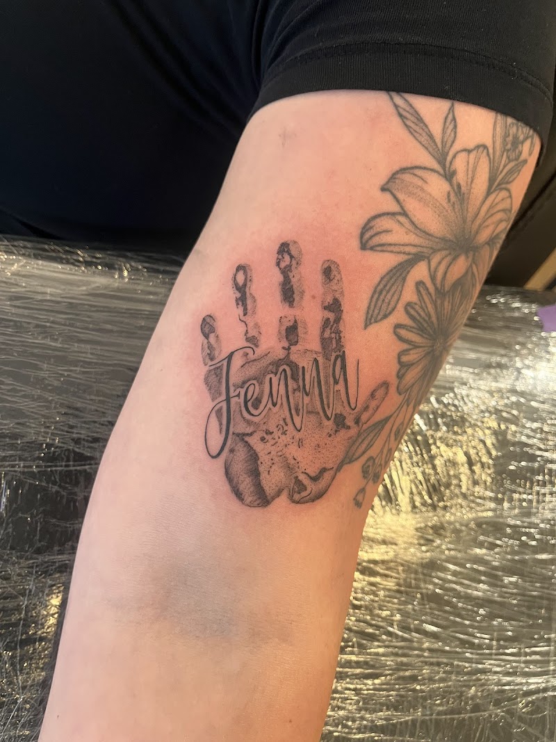 Handafdruk met de naam 'Jenna' in sierlijke letters op de bovenarm.