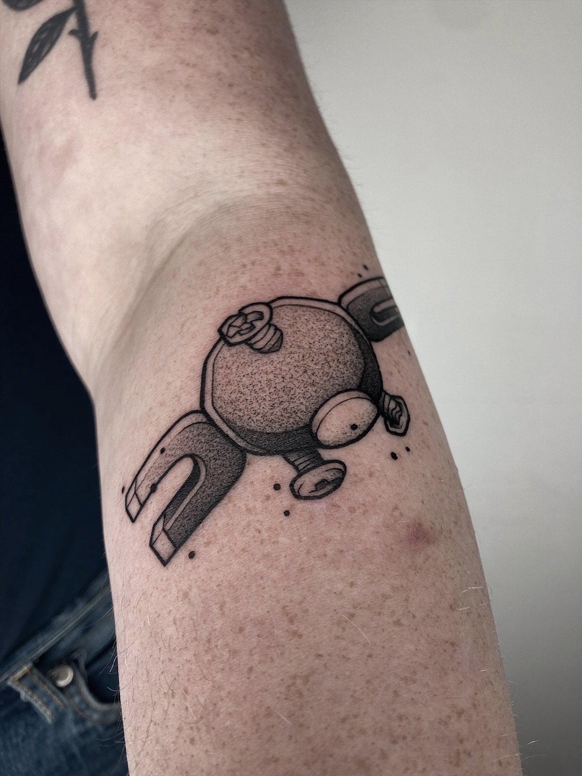 Zwart-wit Magnemite Pokémon tattoo met dotwork shading op de bovenarm.