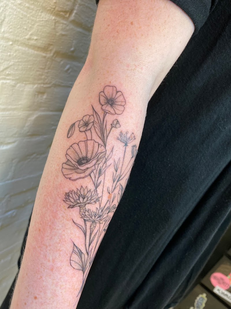 Fineline bloemenboeket met klaprozen en korenbloemen op onderarm.