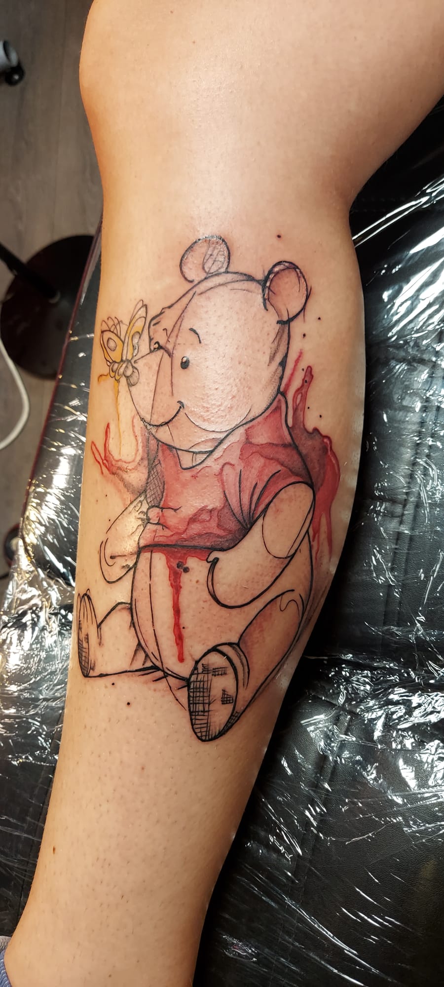 Winnie de Poeh met vlinder in schets en aquarel stijl op onderbeen.