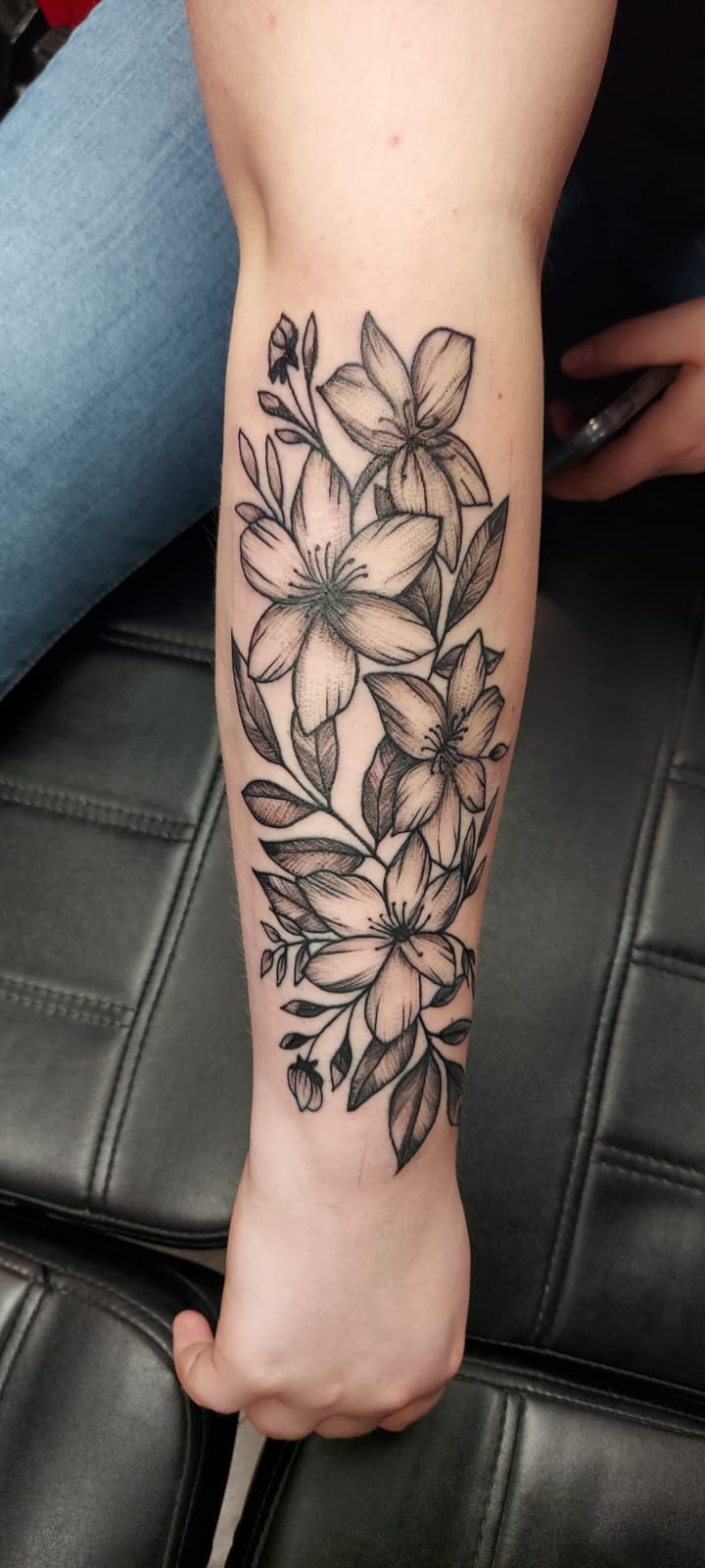Fineline bloemen tattoo met lelies op onderarm.