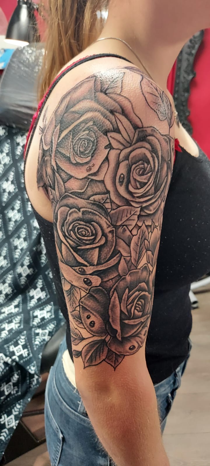 Grote zwart-wit tatoeage van een bos rozen met bladeren op de bovenarm.