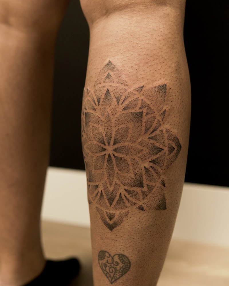 Dotwork mandala tattoo op kuit, met klein hartje eronder.