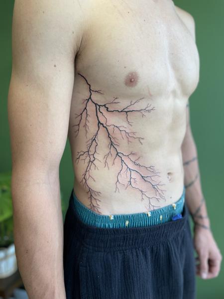 Grote zwarte bliksemschicht tattoo op de ribben.