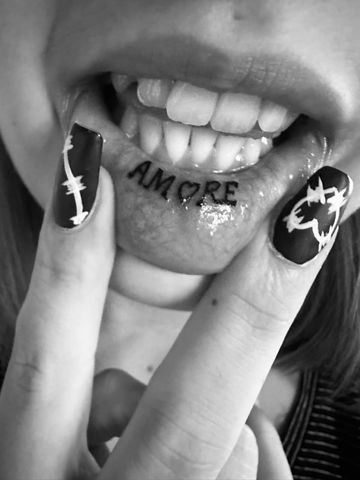 Zwart-wit foto van 'AMORE' tattoo aan de binnenkant van de onderlip.