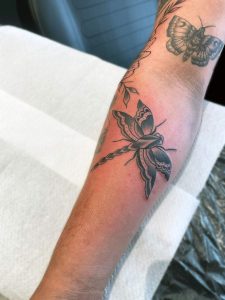 Zwart-wit libelle en vlinder tattoo op onderarm.
