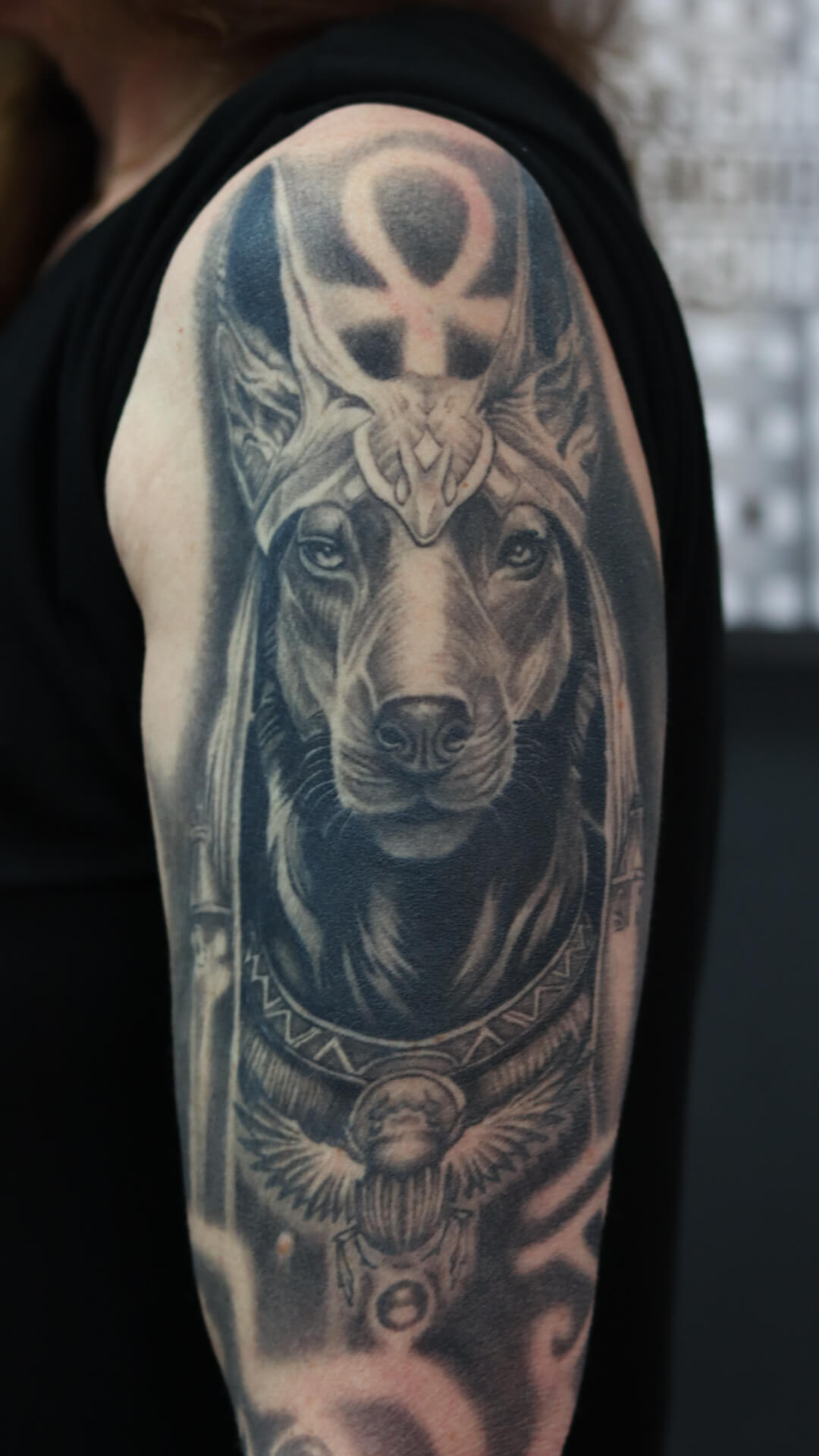 Realistische Anubis tattoo met Ankh en scarabee op bovenarm.