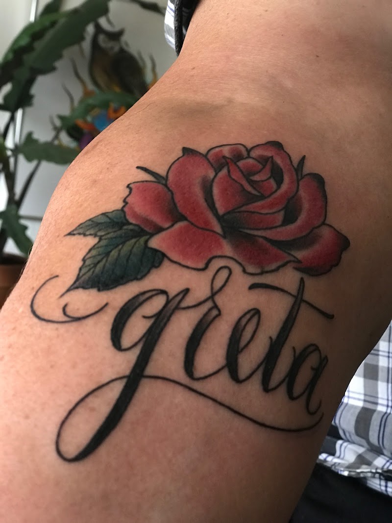 Rode roos met de naam 'Greta' in sierlijk schrift op de bovenarm.