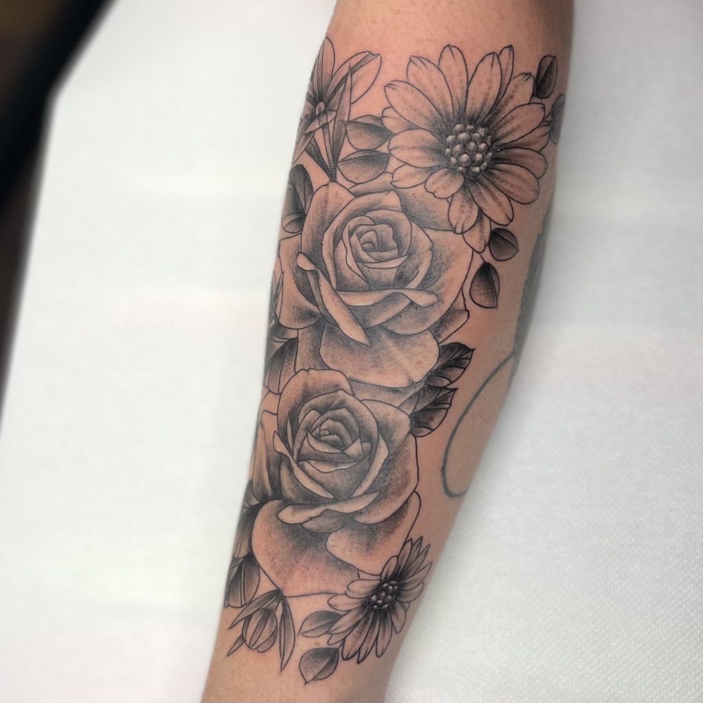 Illustratieve bloemen tattoo met rozen en madeliefjes op onderarm.