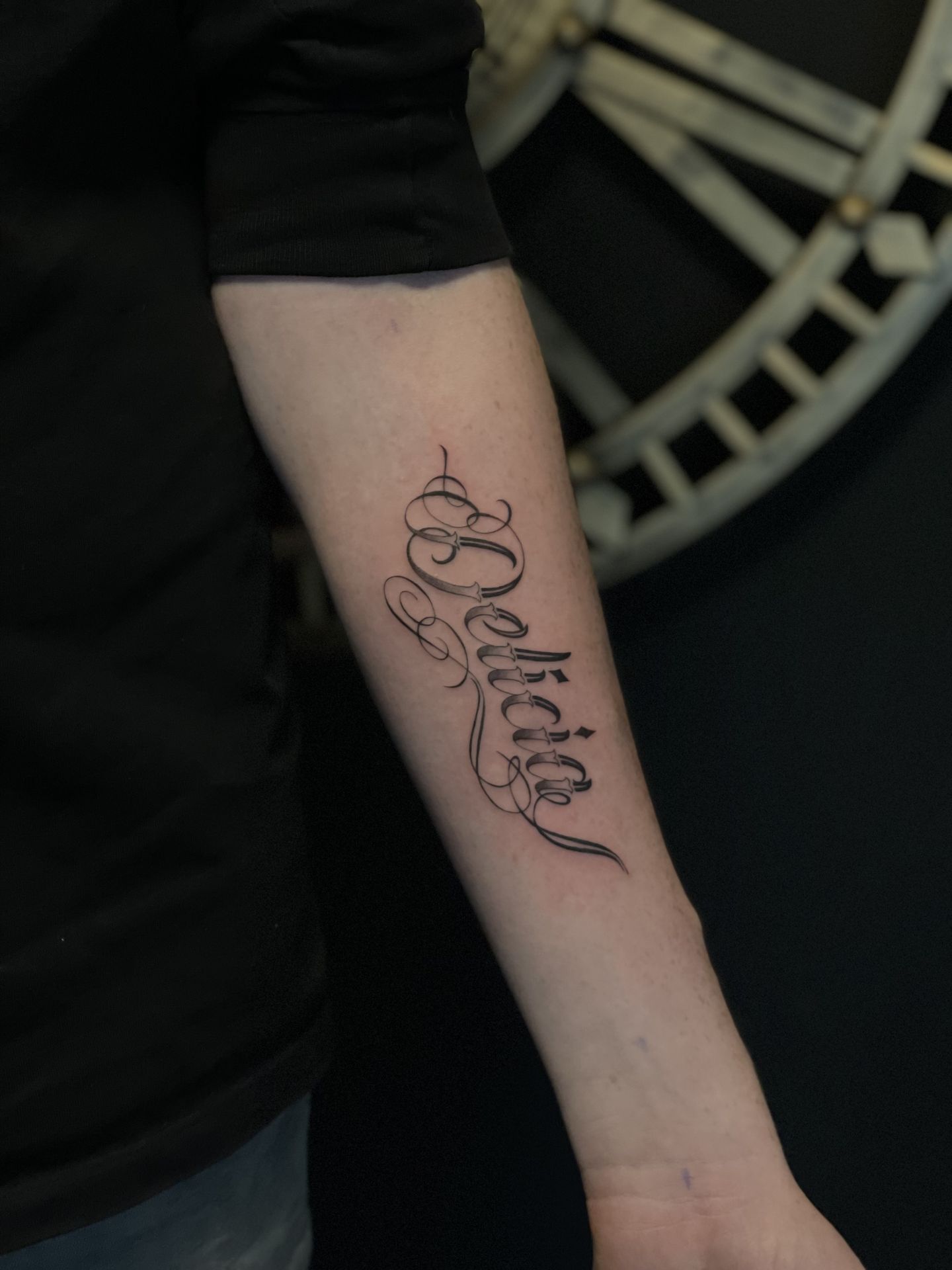 Elegante 'Delicia' naam tattoo in sierlijk schrift op de onderarm.