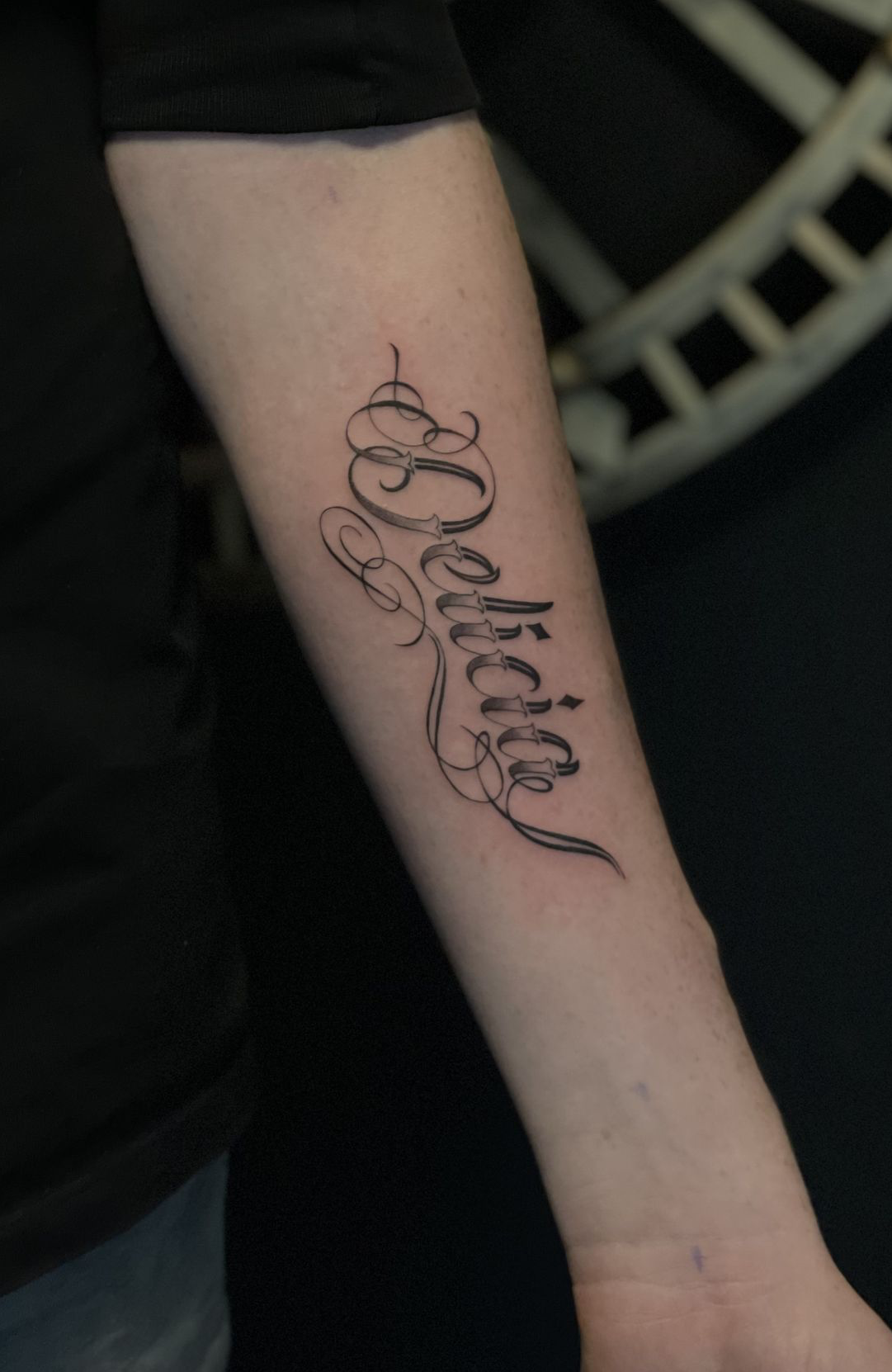 Elegante script tattoo van het woord 'Believe' op de onderarm.