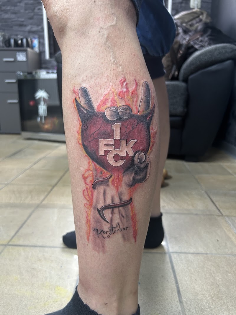 Kleurrijke tattoo van een duivelshart met '1. FCK' logo, vlammen en een hand.