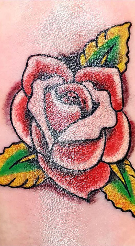 Close-up van een traditionele roos tattoo in rood, groen en geel.