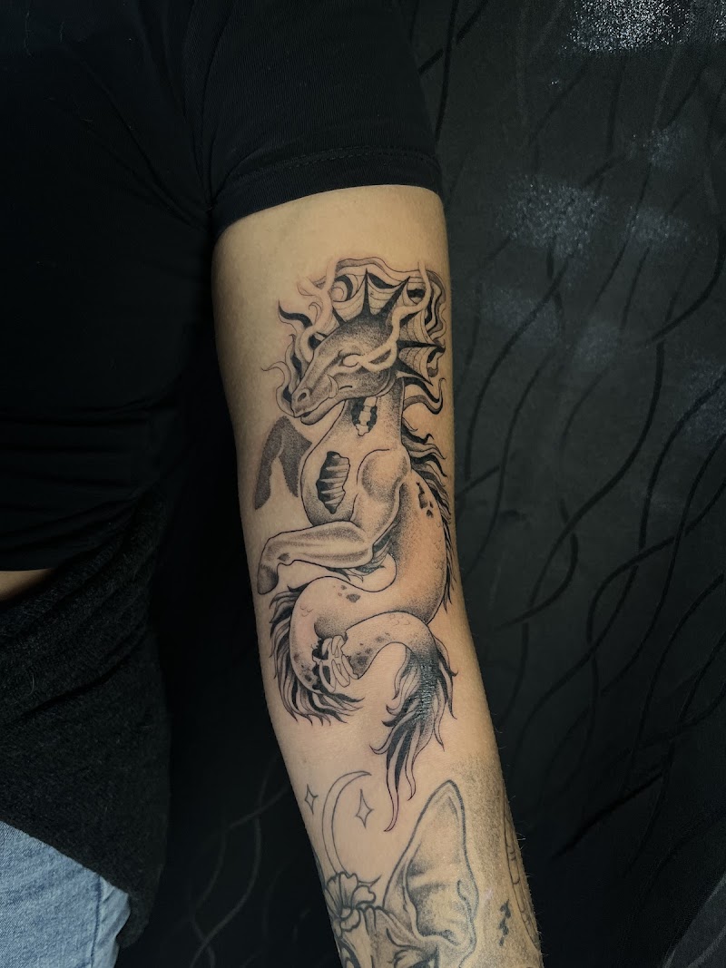 Zwart-wit tattoo van een mythisch zeepaard/draak wezen op de bovenarm.