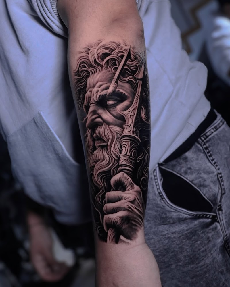 Realistische zwart-wit tattoo van Poseidon met drietand op onderarm.