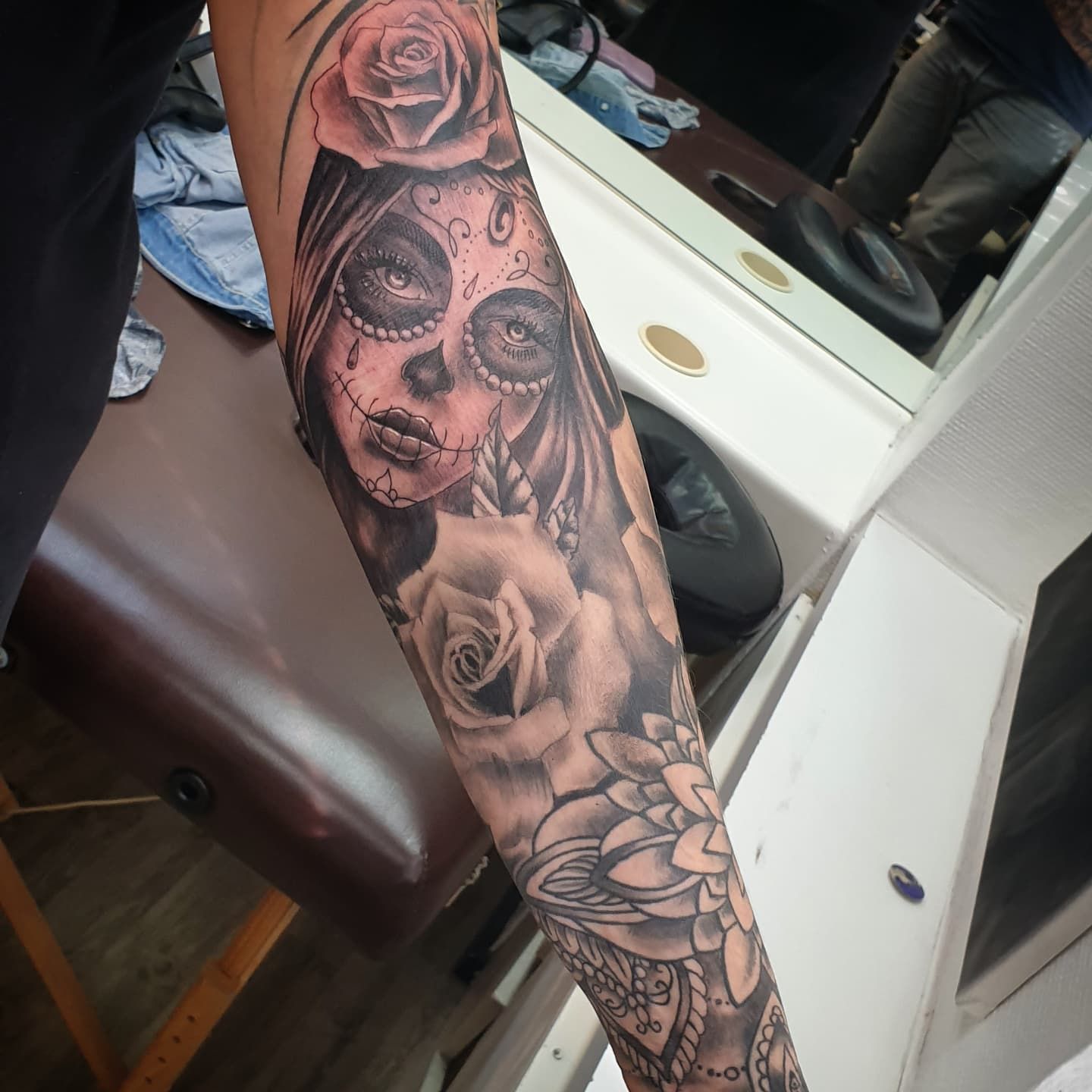 Zwart-grijze tattoo van een Day of the Dead vrouw met rozen op de onderarm.