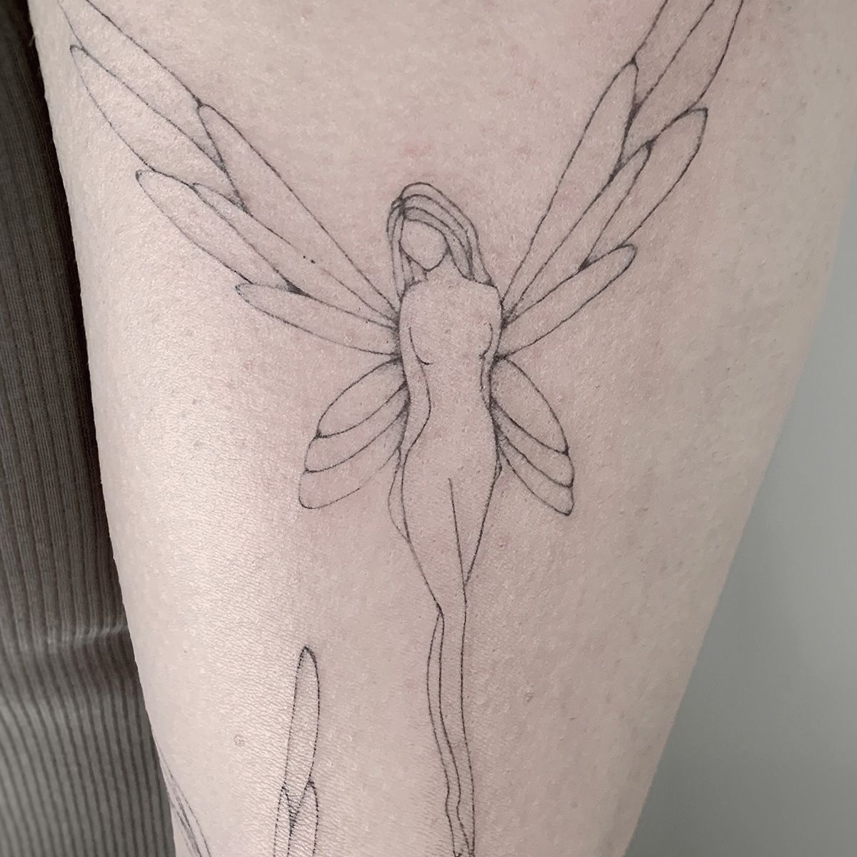 Fineline tattoo van een fee op de bovenarm.