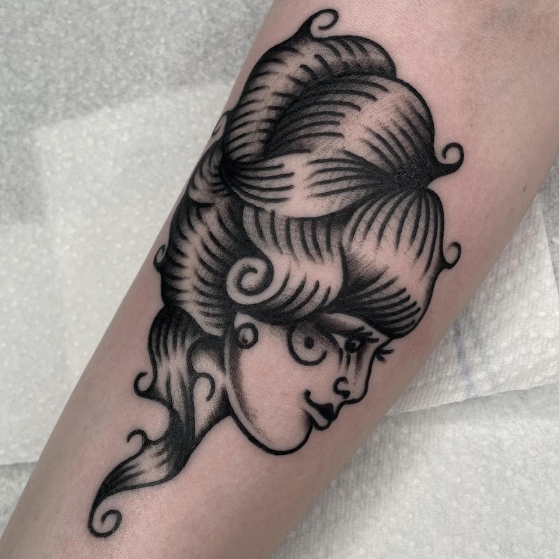 Zwart-wit traditionele tattoo van een vrouwenhoofd met gestileerd haar.