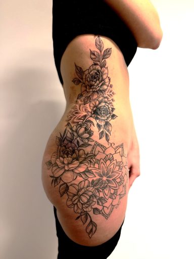 Grote fineline tattoo van bloemen en mandala op de zij en heup.
