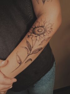 Fineline zonnebloem tattoo op de onderarm.