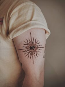 Blackwork tattoo van een oog in een zon op de bovenarm.