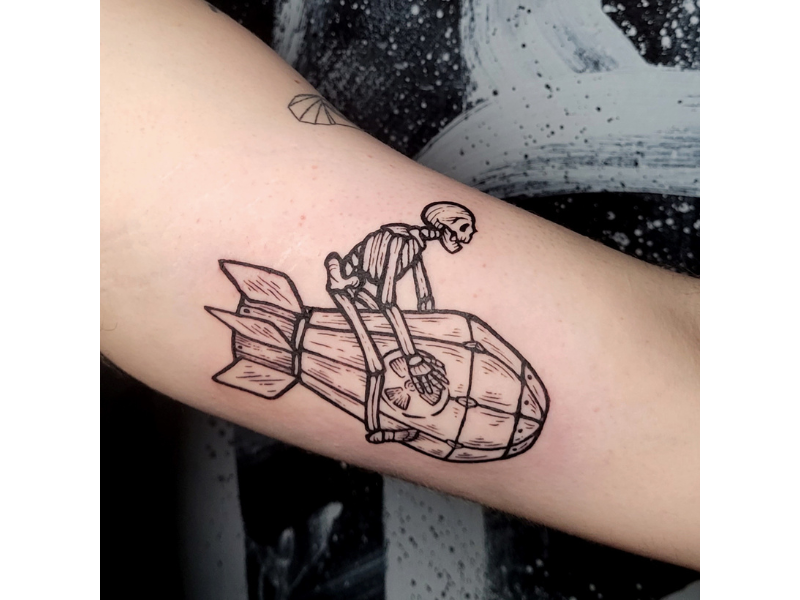 Zwart-wit lijnwerk tattoo van een skelet dat op een bom rijdt.