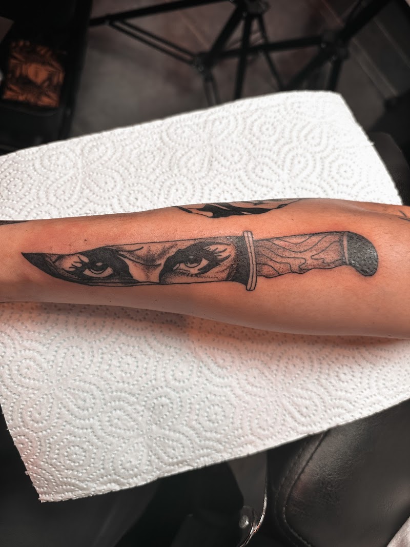 Zwart-wit tattoo van een mes met vrouwenogen op het lemmet.