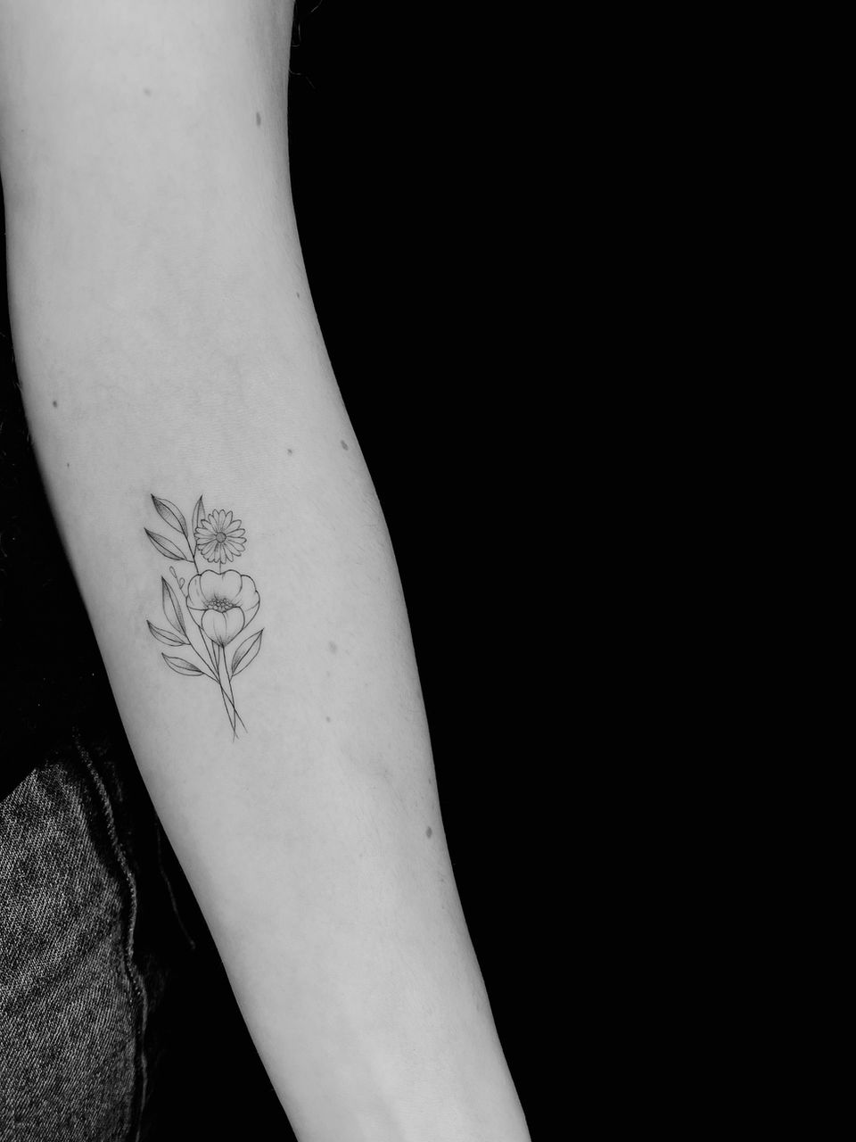 Fijne lijntekening van een klaproos en madeliefje op de onderarm.