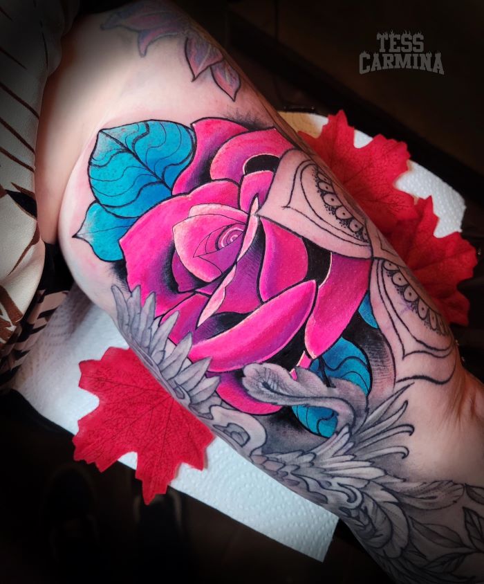 Grote roze roos met blauwe bladeren en grijze ornamenten op de bovenarm.