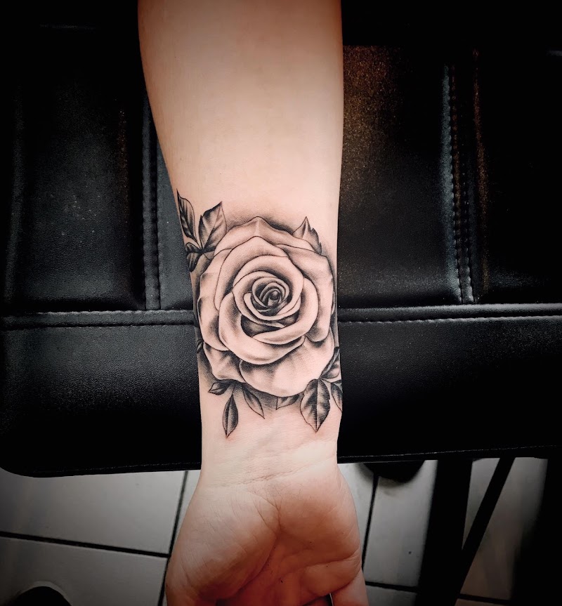 Zwart-grijze roos tattoo op de pols met bladeren.