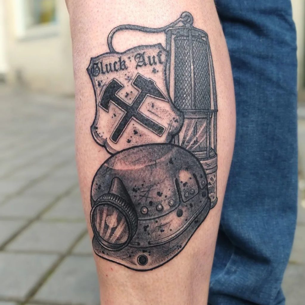 Blackwork tattoo van een mijnwerkershelm, lamp en schild met 'Glück Auf'.