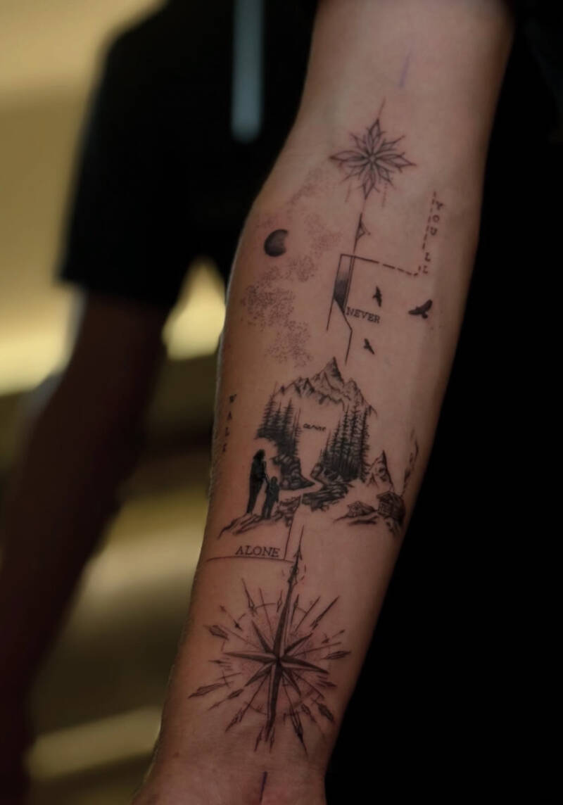 Fineline tattoo met kompas, bergen, figuren en tekst 'NEVER ALONE'.