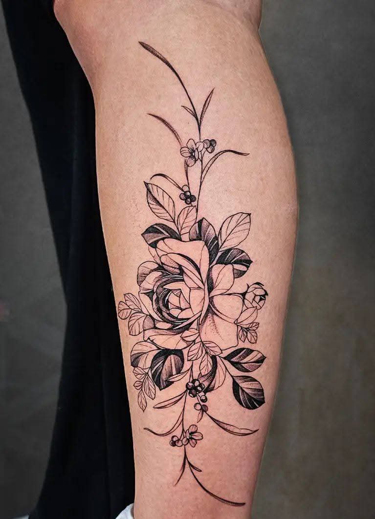 Elegante blackwork bloemen tattoo met een roos en bladeren op het onderbeen.