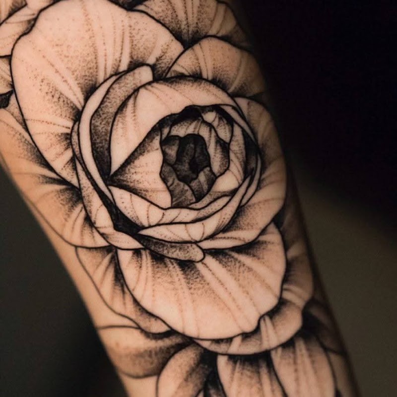 Grote zwart-wit bloem tattoo met dotwork schaduw op de bovenarm.