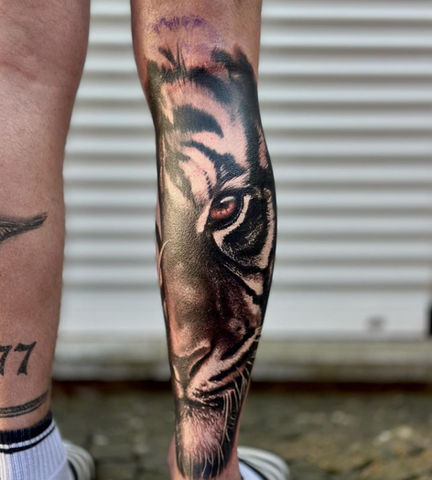 Realistische tijgerkop tattoo op onderbeen, zwart-wit met gekleurd oog.
