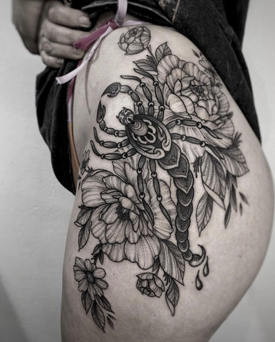 Grote blackwork schorpioen met bloemen op heup en bovenbeen.