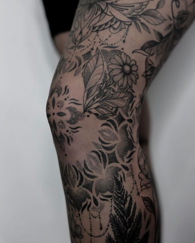 Gedetailleerde blackwork tattoo met bloemen en geometrische patronen op de knie.