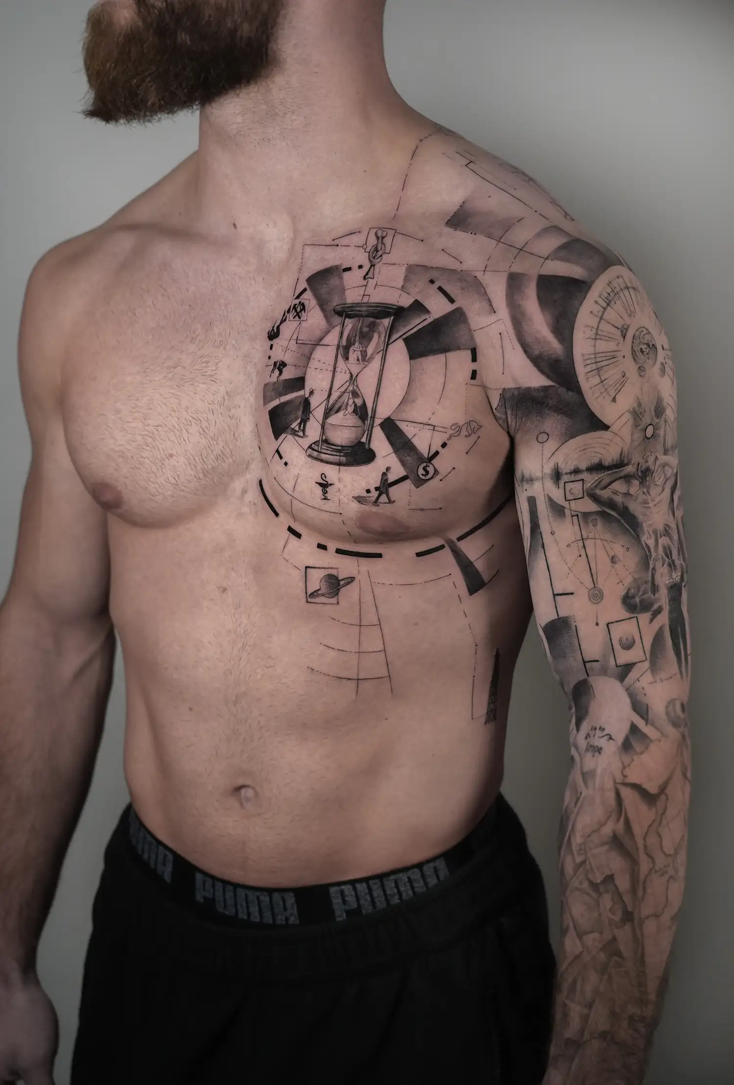 Grote geometrische en realistische tattoo op borst en arm met zandloper en klok.