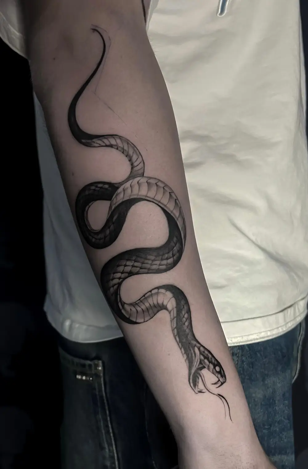 Zwart-wit slang tattoo op onderarm, kronkelend met open bek.