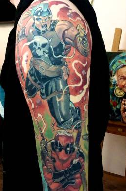 Kleurrijke comic tattoo van Punisher-vrouw en Deadpool op bovenarm.