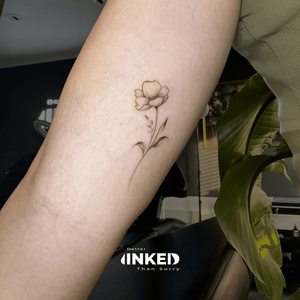 Subtiele fineline bloem tattoo op de achterkant van de bovenarm.