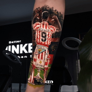 Realistische tattoo van voetballer met trofee op onderbeen.