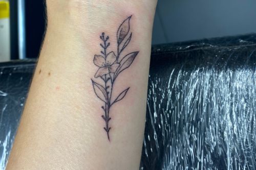 Fineline bloem en bladeren tattoo op de pols.