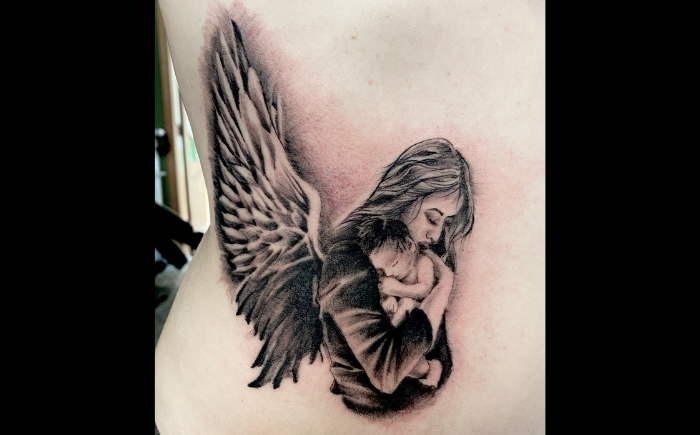 Realistische tattoo van een engel die een baby vasthoudt op de ribben.