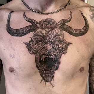 Grote blackwork tattoo van een gehoornde demonenkop op de borst.