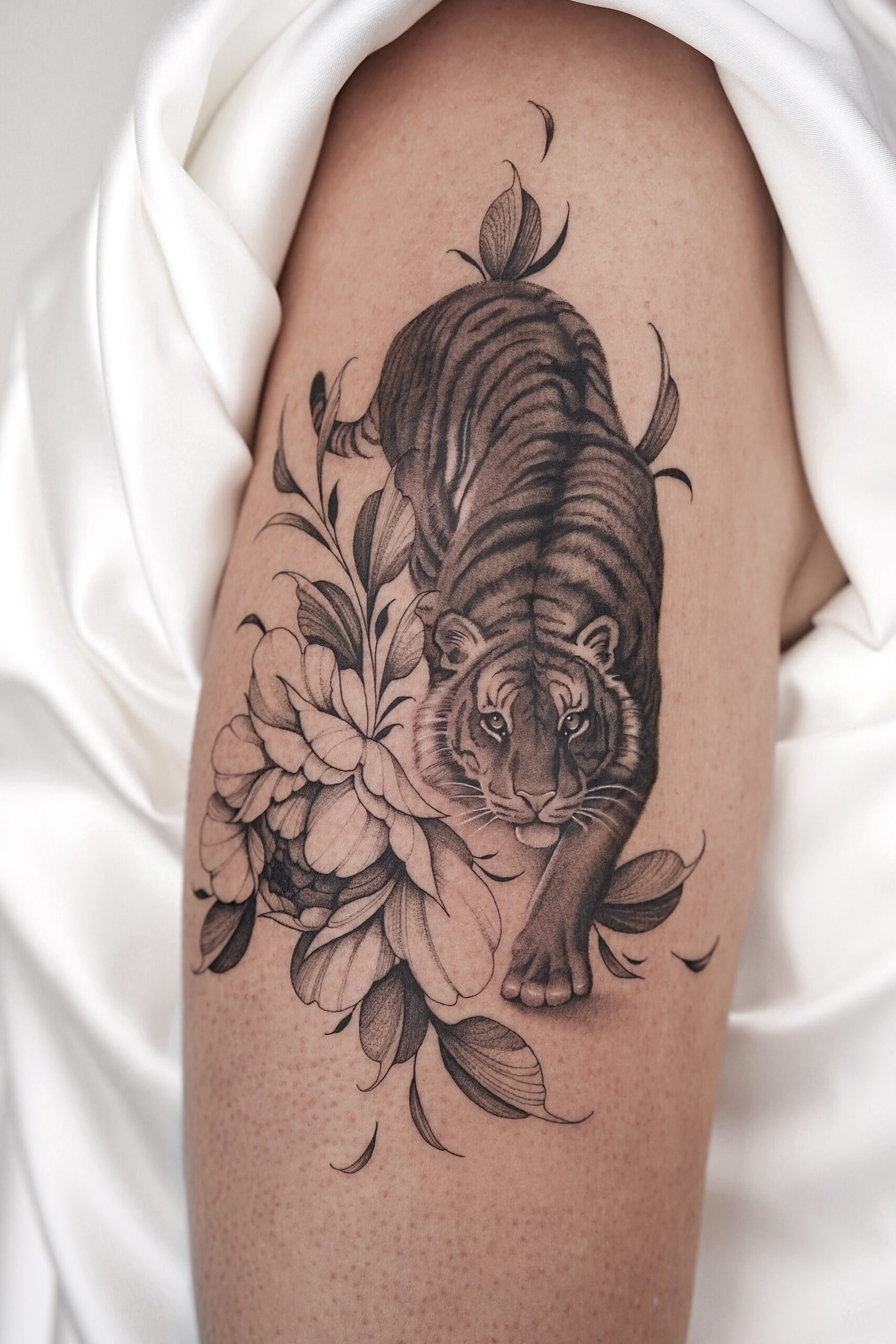 Zwart-wit tattoo van een tijger die door grote bloemen sluipt op de bovenarm.