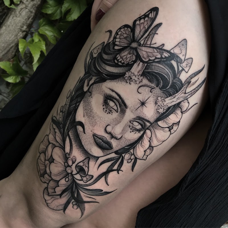 Blackwork tattoo van een vrouwengezicht met hoorns, paddenstoelen en een vlinder.