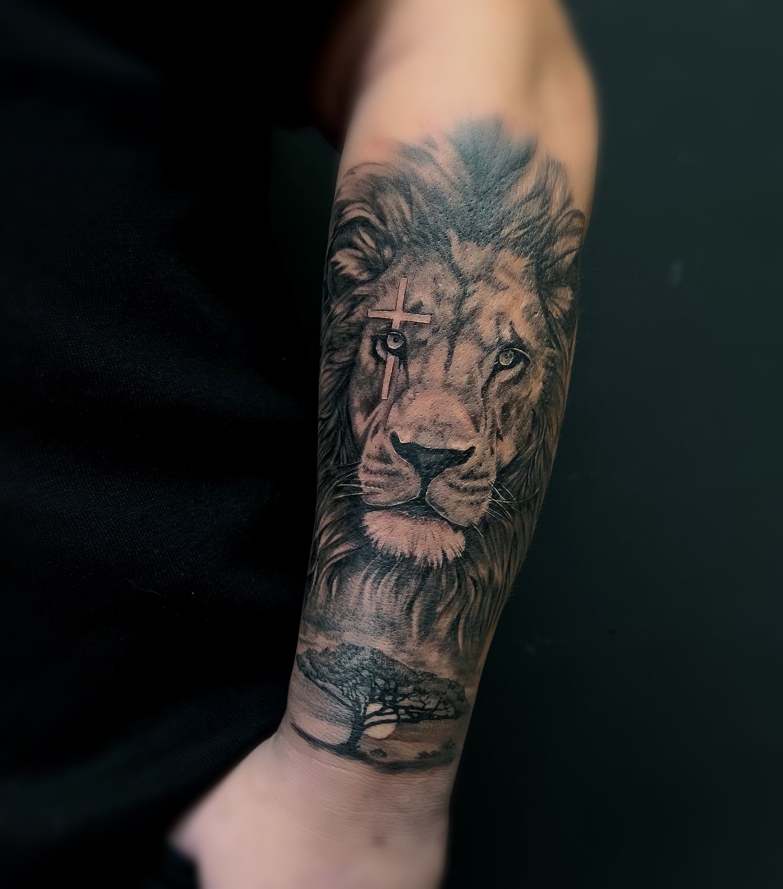 Realistische leeuw met kruis en savanne landschap op onderarm.